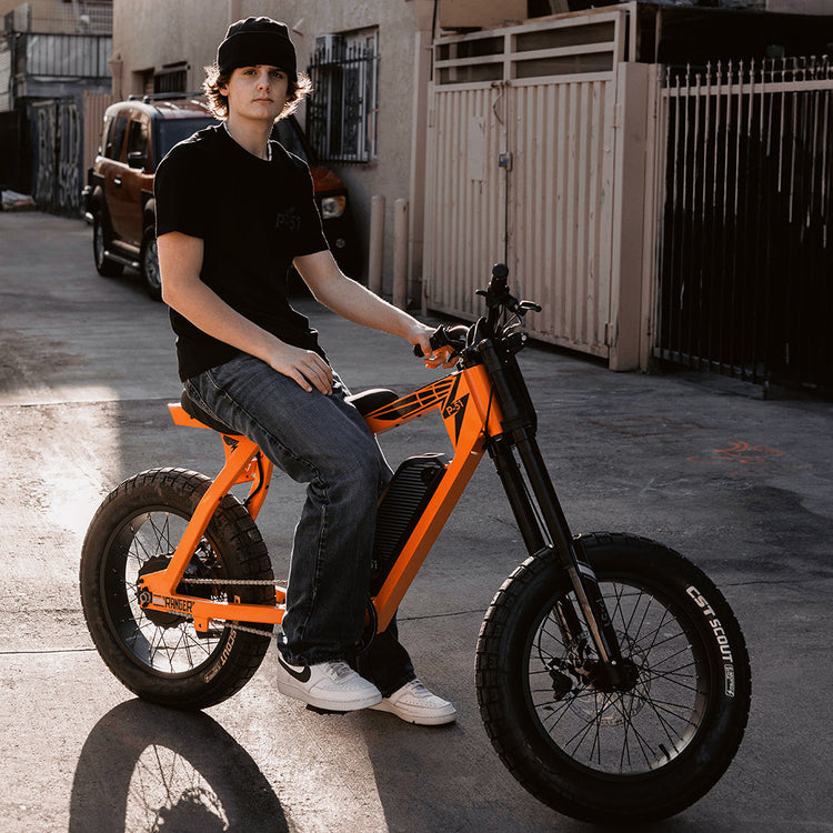 Person sitting on an orange electric bike, P-51 Ranger,  in an urban setting